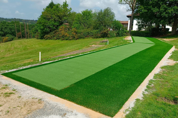 Greenwich Outdoor tee line consisting of one continuous green synthetic grass strip surrounded by trees