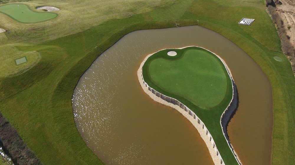 Greenwich Aerial view of a vibrant green synthetic grass island in a natural pond on a golf course