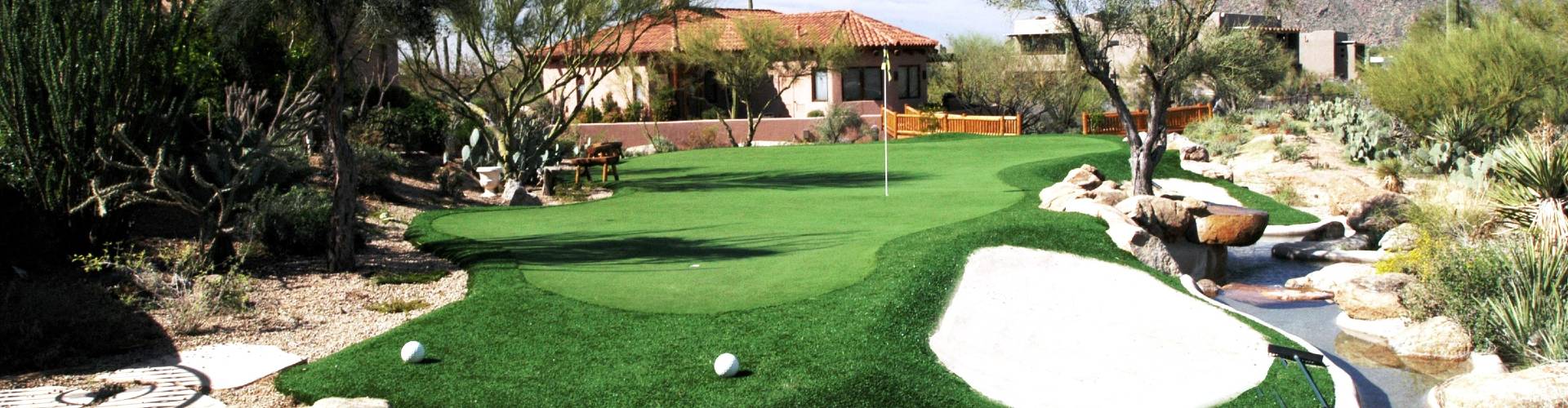 Southwest Greens putting green turf in a desert backyard with sand traps, golf flag, and Southwestern home backdrop